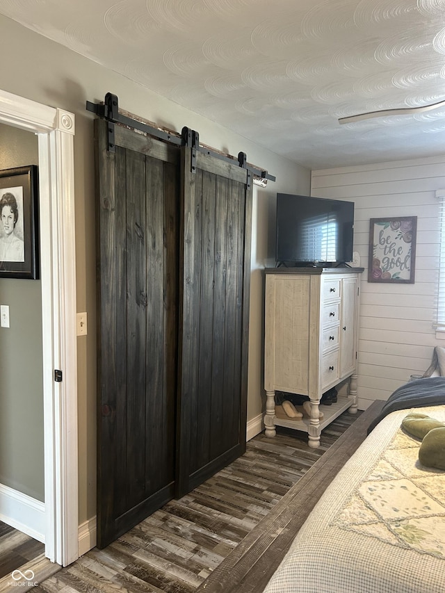 bedroom featuring a barn door, dark wood-type flooring, and baseboards