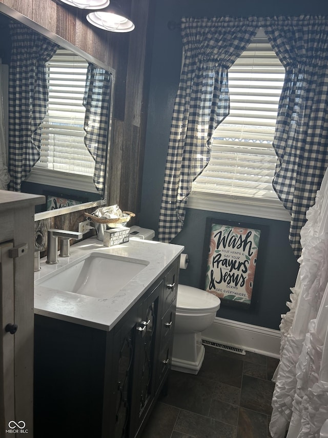 half bath featuring stone finish flooring, baseboards, vanity, and toilet