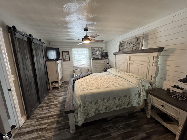 bedroom with a barn door, dark wood finished floors, and a ceiling fan