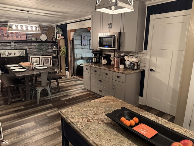 kitchen featuring brick wall, stainless steel microwave, dark wood finished floors, and gray cabinetry