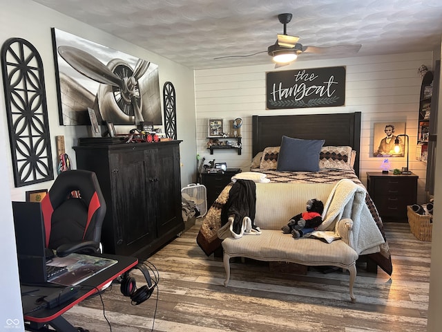 bedroom with ceiling fan, wood walls, wood finished floors, and a textured ceiling