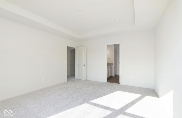 unfurnished bedroom featuring ensuite bath, carpet, and a raised ceiling