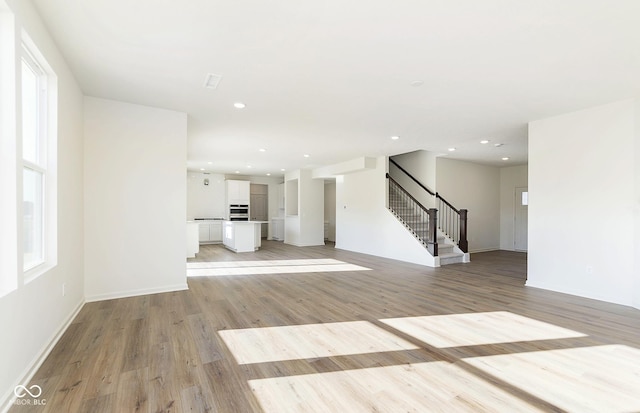 unfurnished living room with recessed lighting, light wood-style flooring, baseboards, and stairs