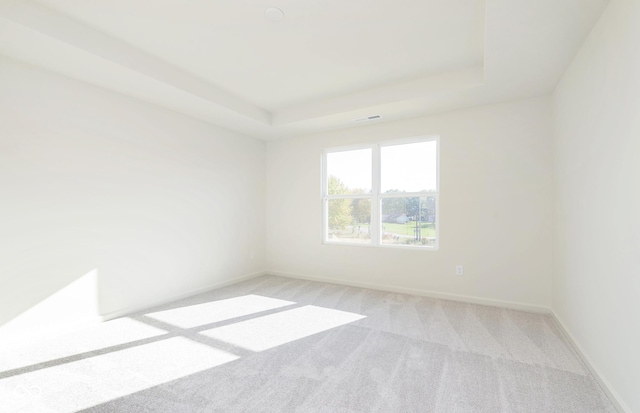 spare room with a raised ceiling, light carpet, visible vents, and baseboards