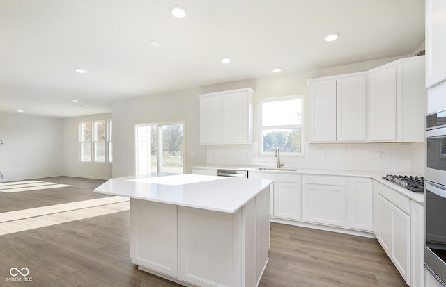 kitchen featuring light wood-style flooring, a kitchen island, a sink, light countertops, and decorative backsplash