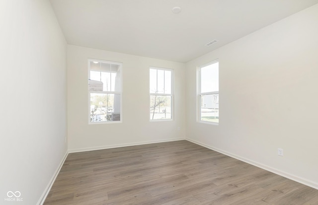 empty room with light wood-type flooring, visible vents, and baseboards