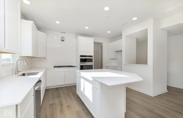 kitchen with light wood finished floors, white cabinets, appliances with stainless steel finishes, a sink, and backsplash