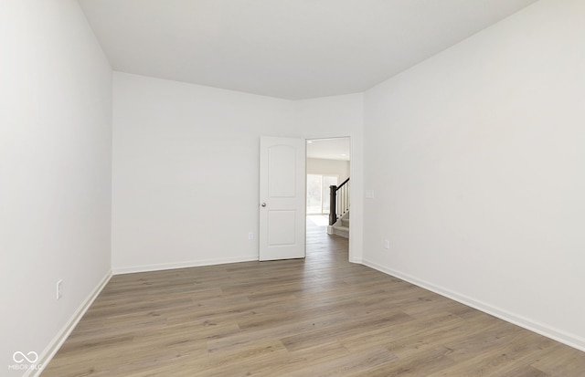 spare room with stairs, baseboards, and light wood-style floors