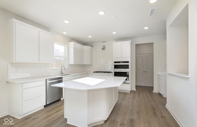 kitchen with stainless steel appliances, a sink, visible vents, light countertops, and backsplash