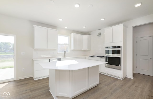 kitchen featuring a sink, light wood-style flooring, backsplash, and stainless steel double oven