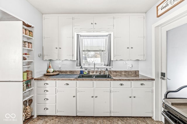 kitchen with dark countertops, a sink, and white cabinets