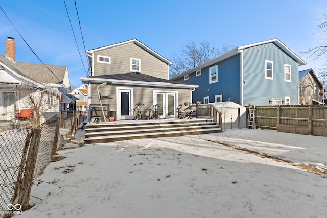 snow covered property featuring an outbuilding, a storage unit, a fenced backyard, and a deck