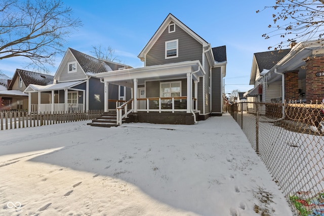 snow covered back of property featuring covered porch and fence