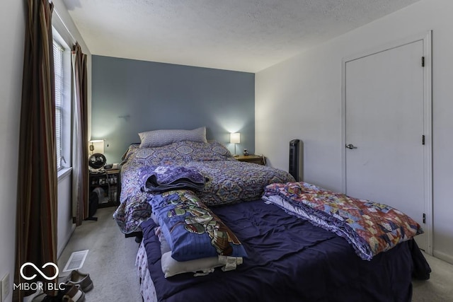 bedroom featuring light carpet, visible vents, and a textured ceiling