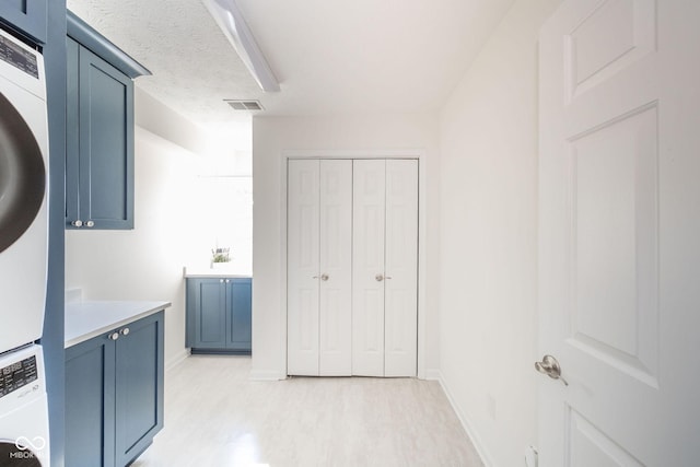 interior space with visible vents, light wood-style floors, stacked washer and clothes dryer, light countertops, and blue cabinetry