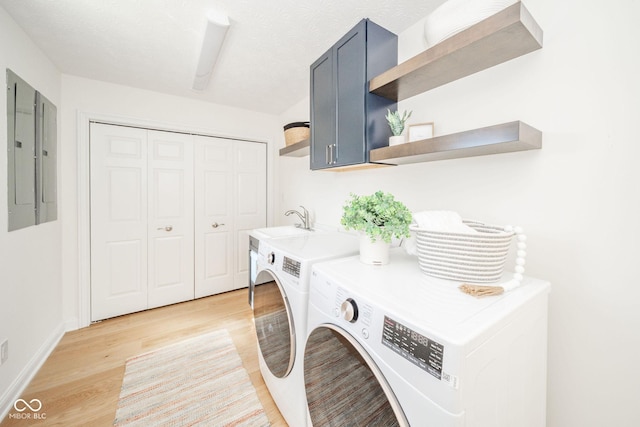 washroom with washing machine and dryer, a sink, cabinet space, electric panel, and light wood finished floors