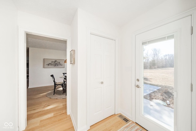 doorway with wood finished floors, visible vents, and baseboards