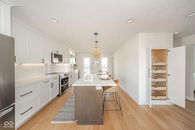 kitchen featuring light countertops, hanging light fixtures, appliances with stainless steel finishes, a kitchen island with sink, and white cabinets