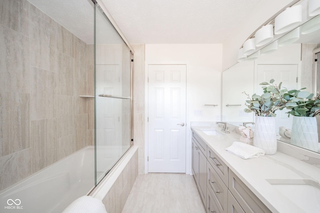 full bath featuring a textured ceiling, bath / shower combo with glass door, double vanity, and a sink