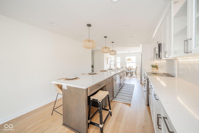 kitchen featuring a breakfast bar, stainless steel appliances, hanging light fixtures, white cabinetry, and a kitchen island with sink