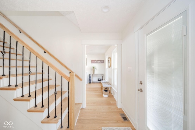 hallway with light wood finished floors, baseboards, stairway, and visible vents