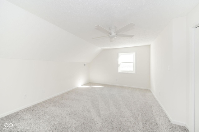 additional living space featuring light carpet, vaulted ceiling, a textured ceiling, ceiling fan, and baseboards