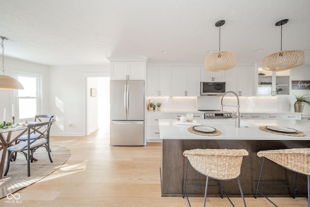 kitchen featuring white cabinets, hanging light fixtures, light wood-type flooring, freestanding refrigerator, and tasteful backsplash