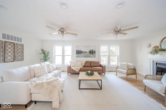 living room with ornamental molding, visible vents, plenty of natural light, and light wood-style flooring