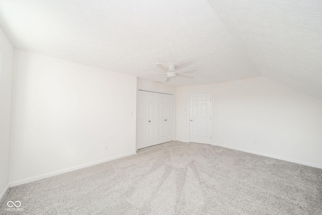 spare room featuring carpet floors, lofted ceiling, a textured ceiling, and baseboards