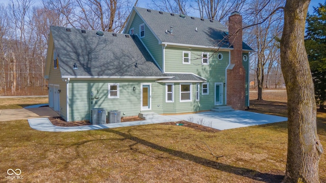 rear view of house with entry steps, a patio, a shingled roof, a yard, and a chimney