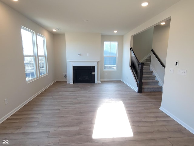 unfurnished living room with a healthy amount of sunlight, light wood finished floors, a fireplace, and stairway