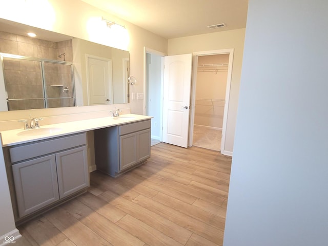 bathroom with visible vents, wood finished floors, a spacious closet, vanity, and a shower stall