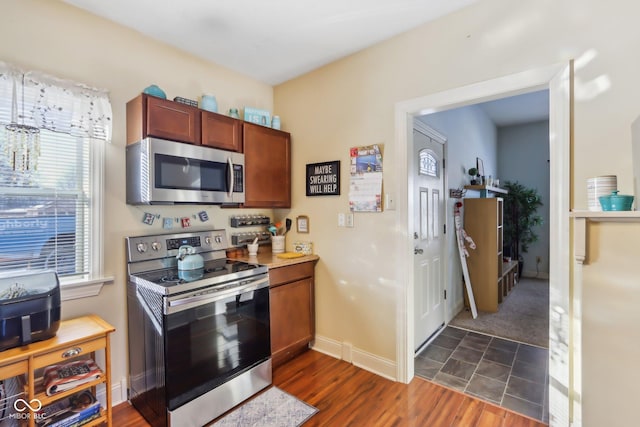 kitchen with dark wood-style flooring, baseboards, light countertops, appliances with stainless steel finishes, and brown cabinets