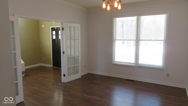 empty room featuring a chandelier, visible vents, baseboards, and wood finished floors