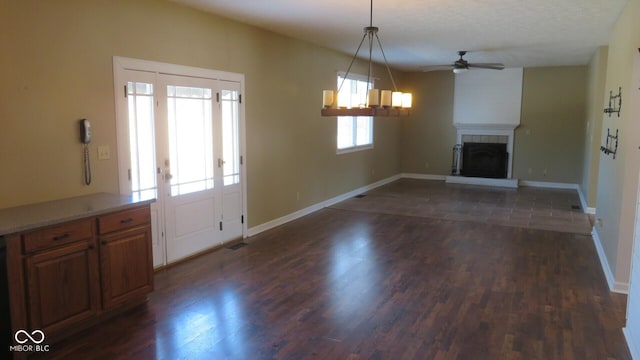 unfurnished living room with a fireplace with raised hearth, ceiling fan, dark wood-type flooring, and baseboards