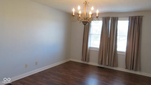 unfurnished room with dark wood-style flooring, a notable chandelier, and baseboards