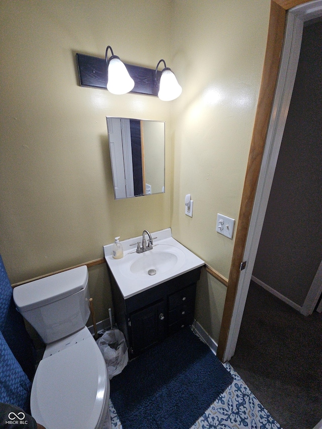 half bath with baseboards, vanity, and toilet