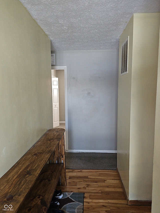 corridor with a textured ceiling, wood finished floors, visible vents, baseboards, and a heating unit