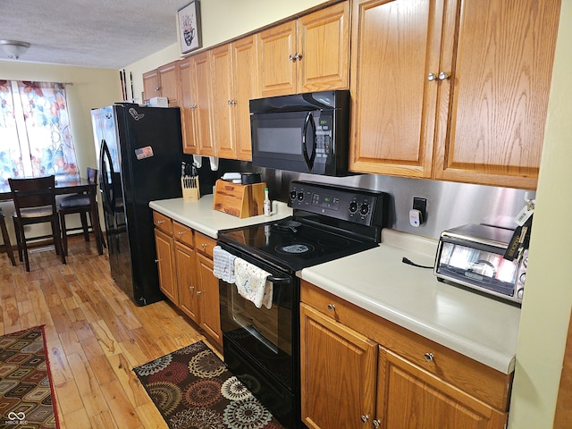 kitchen featuring light wood-style floors, light countertops, a textured ceiling, and black appliances