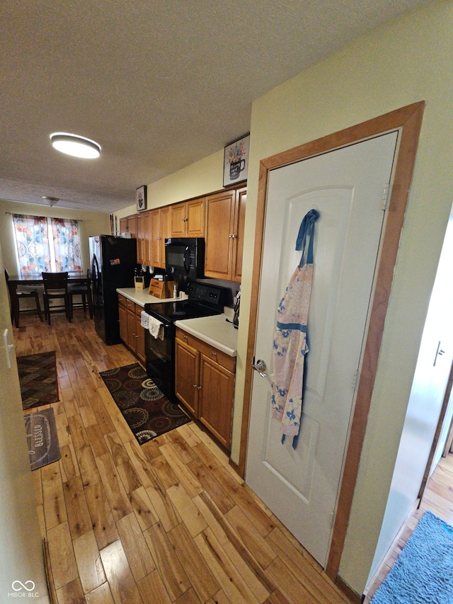 kitchen featuring brown cabinets, light countertops, a textured ceiling, light wood-type flooring, and black appliances