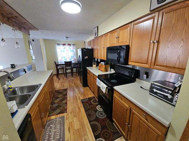 kitchen with a sink, light wood-style floors, light countertops, brown cabinets, and black appliances