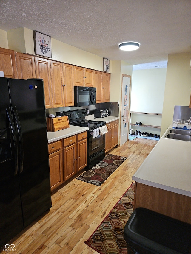 kitchen featuring light wood finished floors, light countertops, a textured ceiling, black appliances, and a sink