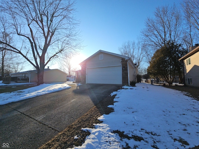 snow covered property featuring a garage, brick siding, and an outdoor structure