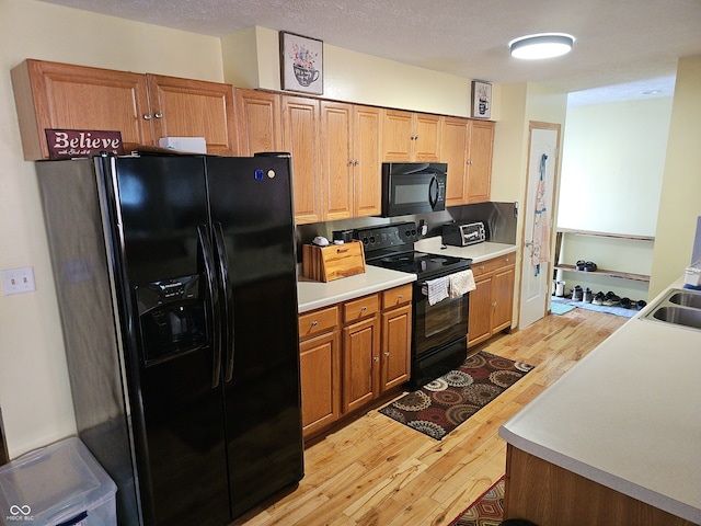 kitchen featuring light countertops, light wood-style flooring, brown cabinetry, a textured ceiling, and black appliances