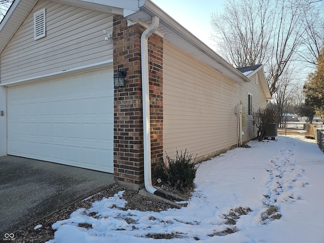 view of snow covered exterior featuring a garage, aphalt driveway, and brick siding