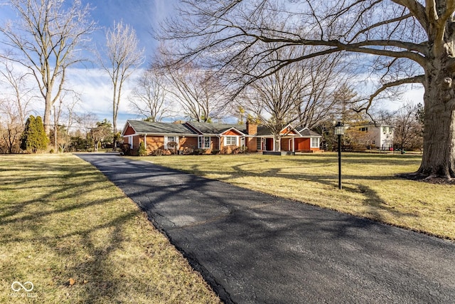 view of front of home featuring aphalt driveway, a front yard, and a chimney