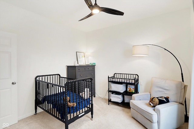 bedroom with light carpet, a nursery area, and a ceiling fan