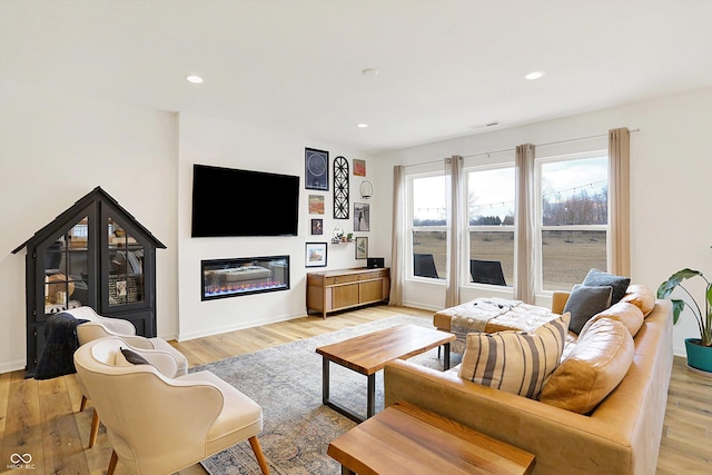 living area featuring light wood finished floors, a glass covered fireplace, and recessed lighting