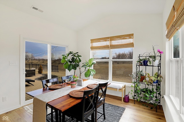 dining area featuring light wood finished floors, visible vents, and vaulted ceiling