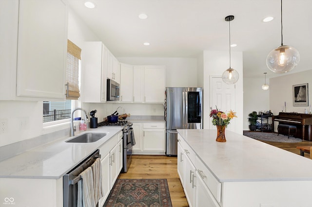 kitchen featuring light wood finished floors, white cabinets, a center island, stainless steel appliances, and a sink